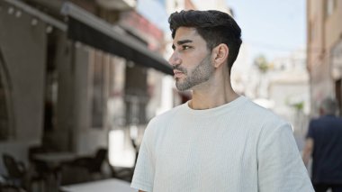 Latin kökenli genç adam ciddi bir ifadeyle sokağa bakıyor.
