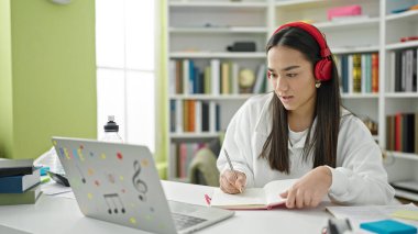 Laptop ve kulaklık kullanan güzel İspanyol kız öğrenci üniversite sınıfında notlar yazıyor.