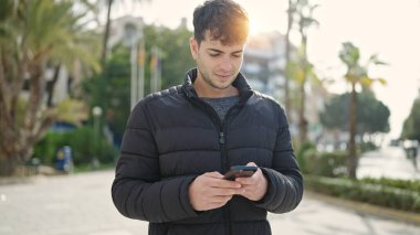 Young hispanic man using smartphone at park