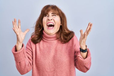 Orta yaşlı İspanyol bir kadın izole edilmiş arka planda duruyor ve başarı için deli ve kızgınlığını kutluyor kollarını kaldırmış, gözlerini kapatmış heyecanlı çığlıklar atıyor. Kazanan konsept 