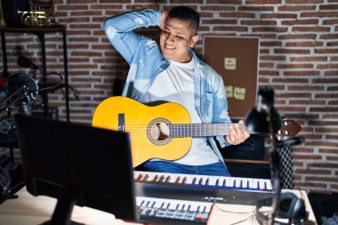 Latin asıllı genç bir adam müzik stüdyosunda klasik gitar çalıyor. Gülümsüyor, el hareketleriyle saçlara dokunuyor, çekici ve modaya uygun poz veriyor. 