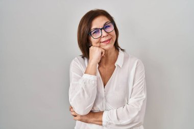 Orta yaşlı İspanyol bir kadın, soyutlanmış arka planda, elleri çenesinde soru sorarken, düşünceli bir ifade takınıyor. Düşünceli bir yüzle gülümsüyor. şüphe kavramı. 