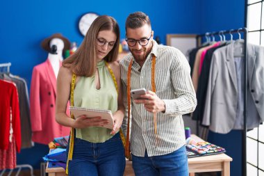 Man and woman tailors using smartphone holding notebook at clothing factory