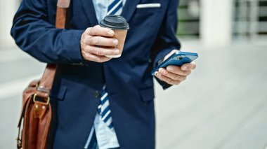 Caddede akıllı telefon kullanan orta yaşlı bir iş adamı kahve tutuyor.