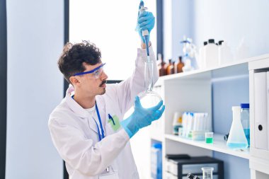 Kafkasyalı genç bilim adamı laboratuarda test tüpüne sıvı döküyor.
