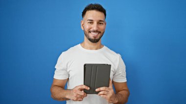 Genç Arap adam kendinden emin bir şekilde mavi arka plan üzerinde dokunmatik ped kullanıyor.