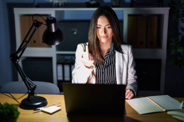 Young brunette woman working at the office at night with laptop showing middle finger, impolite and rude fuck off expression 