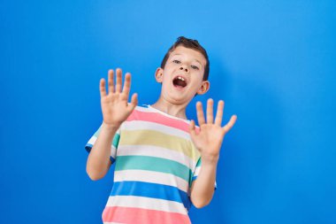 Mavi arka planda korkmuş ve korkudan dehşete düşmüş beyaz bir çocuk. El kol hareketi yapmayı kes, şok içinde bağır. panik konsepti. 