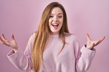 Pembe arka planda duran genç beyaz kadın, başarı için çıldırıyor ve çıldırıyor kollarını kaldırıyor ve gözleri kapalı heyecanla bağırıyor. Kazanan konsept 