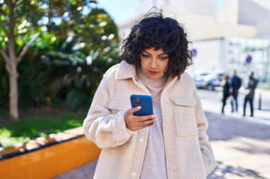 Genç, güzel, İspanyol bir kadın parkta akıllı telefon kullanıyor.