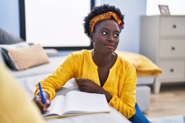 Genç Afrikalı Amerikalı kadın deftere yazı yazıyor. Evinde yerde oturuyor.