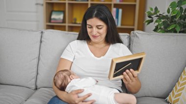 Anne ve bebek kanepede oturmuş, evdeki kareye bakıyorlar.