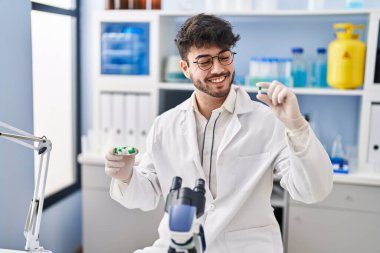 Genç İspanyol bilim adamı gülümseyerek laboratuvarda kendine güvenen haplar tutuyor.