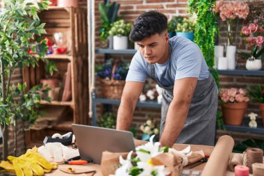 Young hispanic man florist using laptop at flower shop