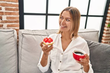 Genç İspanyol kadın evdeki kanepede kahvaltı yapıyor.