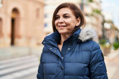 Orta yaşlı bir kadın sokakta kendinden emin bir şekilde gülümsüyor.