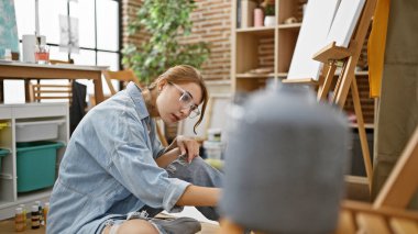 Genç kadın ressam resim çiziyor ve resim stüdyosunda düşünüyor.