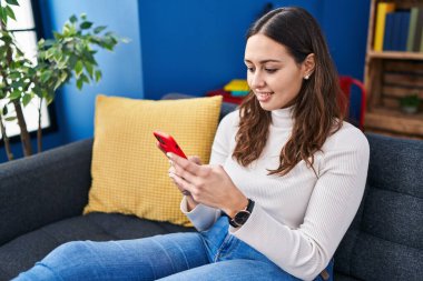 Evdeki kanepede uzanmış akıllı telefon kullanan genç, güzel İspanyol kadın.