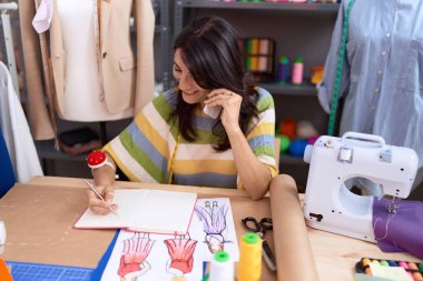 Orta yaşlı İspanyol kadın terzi atölyedeki defterde akıllı telefon yazısıyla konuşuyor.