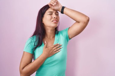 Genç İspanyol kadın pembe arka planda duruyor. Hastalık, ateş, grip ve virüs için alnına dokunuyor. 