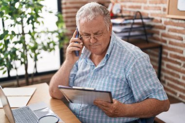 Middle age grey-haired man business worker talking on smartphone reading document at office