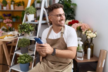 Çiçekçide akıllı telefon kullanarak gülümseyen İspanyol çiçekçi.