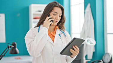 Genç, güzel İspanyol kadın doktor dokunmatik ped kullanıyor. Klinikte akıllı telefondan konuşuyor.