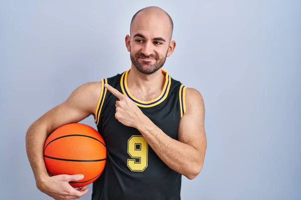 年轻的秃头男子 留着胡子 身穿篮球服 手指头指向旁边的广告 严肃而沉着 — 图库照片