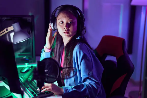Young chinese woman streamer playing video game using computer at gaming room