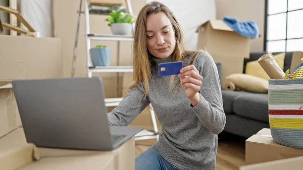Young caucasian woman shopping with laptop and credit card sitting on floor at new home