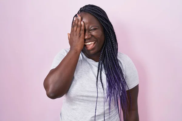 手で片目を覆うピンクの背景の上に立っている若いアフリカの女性 顔に自信を持って笑顔と驚きの感情 — ストック写真