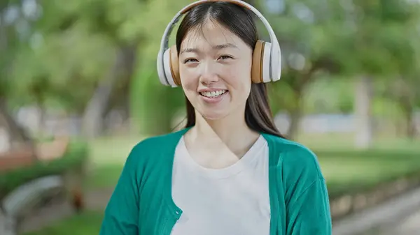 Young chinese woman listening to music smiling at park