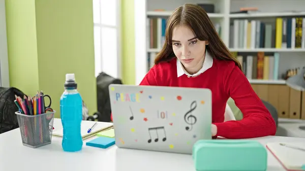 Young hispanic woman student using laptop with relaxed expression at library university