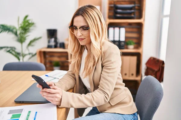 Young blonde woman business worker smiling confident using smartphone at office