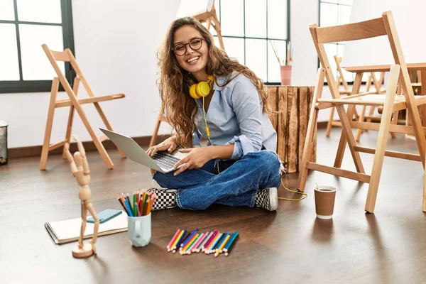 若い美しいヒスパニック女性アーティスト使用してノートパソコンで床に座ってアートスタジオ — ストック写真