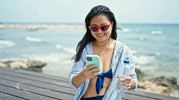 Młoda Chinka Turystka Pomocą Smartfona Trzymając Butelkę Wody Nad Morzem — Zdjęcie stockowe