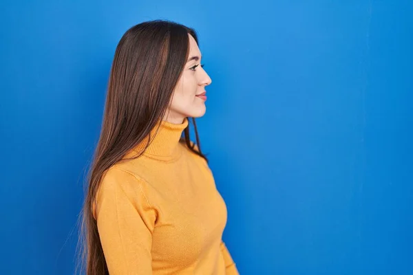 Nuori Brunette Nainen Seisoo Sininen Tausta Etsii Sivuun Rentoutua Profiili — kuvapankkivalokuva