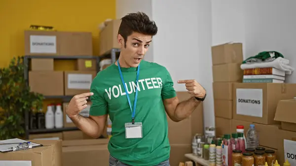 Young Hispanic Man Pointing Volunteer Uniform Smiling Charity Center — Stock Photo, Image