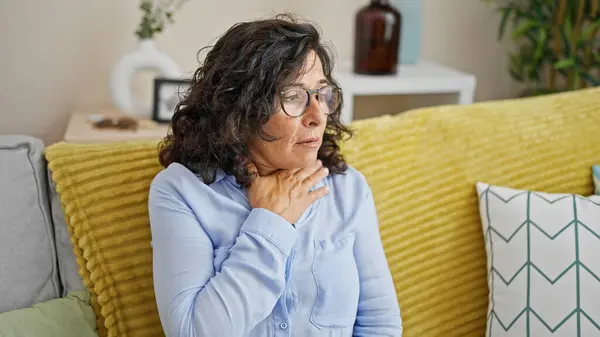 Middle age hispanic woman sitting on sofa suffering anxiety attack at home