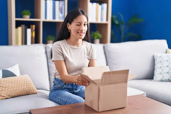 stock image Young hispanic woman opening cardboard box winking looking at the camera with sexy expression, cheerful and happy face. 