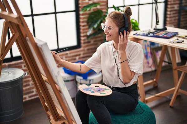 Young blonde woman artist listening to music drawing at art studio