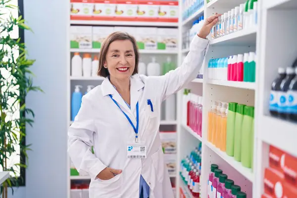 Middle Age Woman Pharmacist Smiling Confident Holding Product Shelving Pharmacy — Zdjęcie stockowe