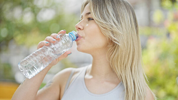 Young blonde woman drinking water at park