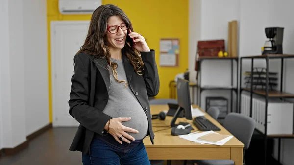 在办公室里 年轻的怀孕女商人正在用智能手机交谈 摸着肚子 — 图库照片