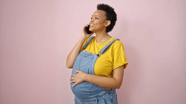 孤立したピンクの背景に笑顔でスマートフォンで話している若い妊婦 — ストック写真