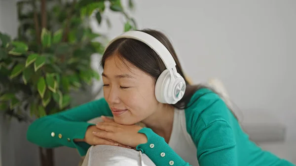 Young chinese woman listening to music sitting on sofa at home