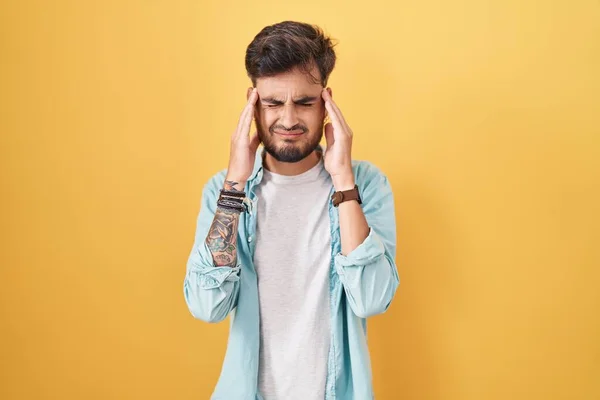 ストレスのため 頭の上に手で黄色の背景に立って入れ墨を持つ若いヒスパニック系の男 片頭痛 — ストック写真