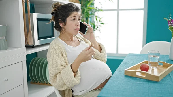 若い妊娠中の女性は ダイニングルームでスマートフォンで話しています — ストック写真