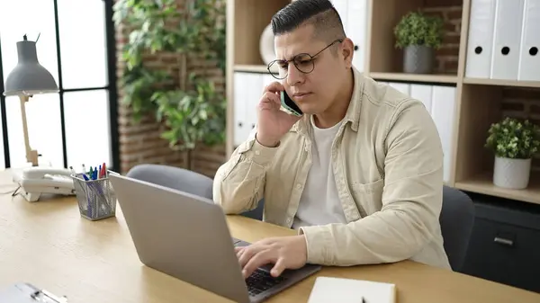 Young Hispanic Man Business Worker Using Laptop Talking Smartphone Office — Stockfoto