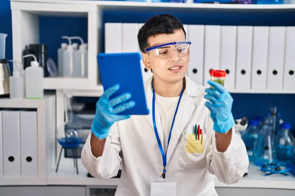 Young non binary man scientist holding urine test tube using touchpad at laboratory